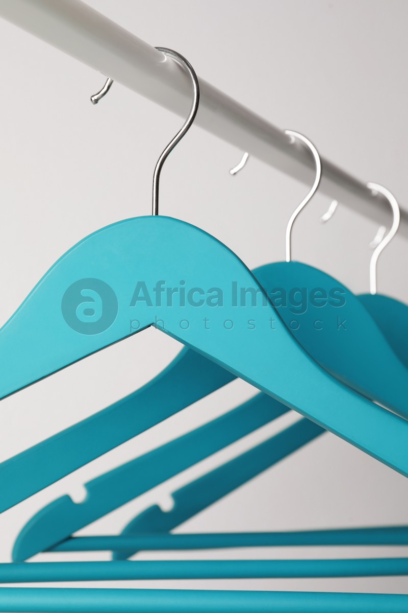 Photo of Empty turquoise clothes hangers on metal rail against light grey background, closeup