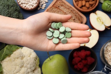 Woman holding pills at table with foodstuff, top view. Prebiotic supplements