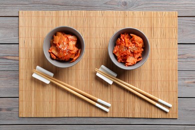 Photo of Bowls of spicy cabbage kimchi and chopsticks on wooden table, flat lay