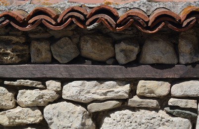 Old stone wall with ceramic tiles roof on sunny day
