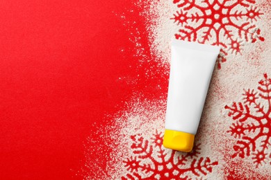 Photo of Winter skin care. Hand cream and snowflake silhouettes made with artificial snow on red background, top view. Space for text