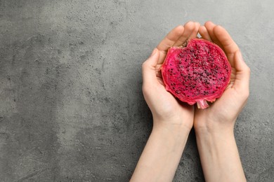 Woman holding fresh cut dragon fruit (pitahaya) on grey table, top view. Space for text
