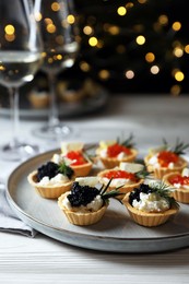 Photo of Delicious tartlets with red and black caviar served on white wooden table against blurred festive lights, closeup. Space for text