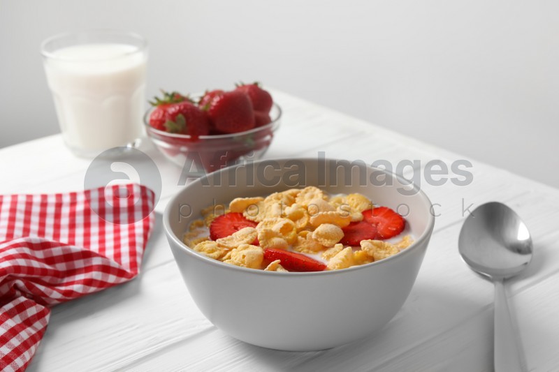 Corn flakes with strawberries in bowl served on white wooden table