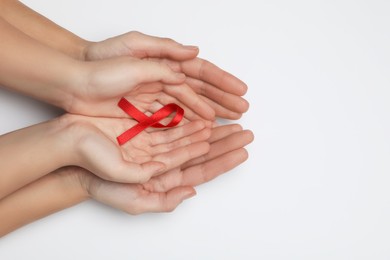 Photo of Woman and girl holding red ribbon on white background, top view. AIDS disease awareness