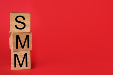 Wooden cubes with abbreviation SMM (Social media marketing) on red background. Space for text