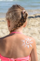 Little girl with sun protection cream on body near sea, back view