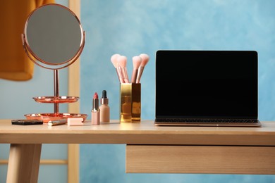 Photo of Wooden table with modern laptop and makeup products in room