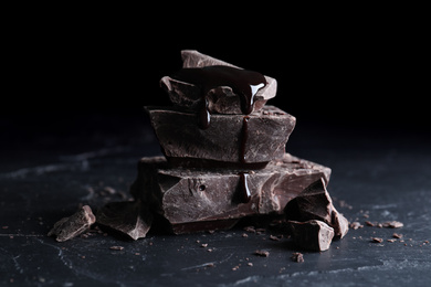 Photo of Pieces of tasty dark chocolate with syrup on black table, closeup