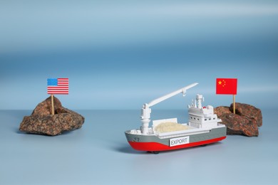 Toy cargo vessel, stones with American and Chinese flags on color background. Export concept