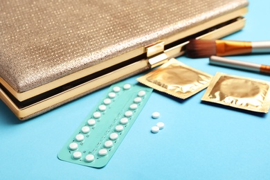 Birth control pills and condoms near clutch on light blue background. Safe sex concept