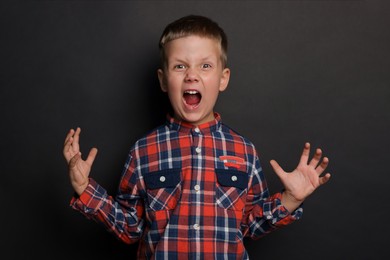 Photo of Angry little boy screaming on black background. Aggressive behavior