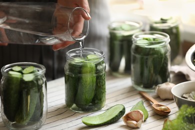 Photo of Woman pouring water into jar with canning cucumbers at table, closeup