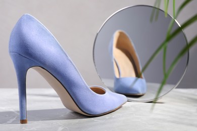 Stylish high heeled shoe in front of mirror on grey table. Vanity concept