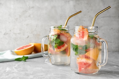 Mason jars of refreshing drink with grapefruit and mint on grey stone table, space for text