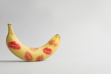 Photo of Banana covered with red lipstick marks on light grey background, space for text. Potency concept
