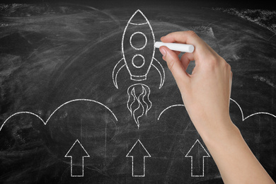 Image of Business startup concept. Woman drawing rocket on blackboard, closeup