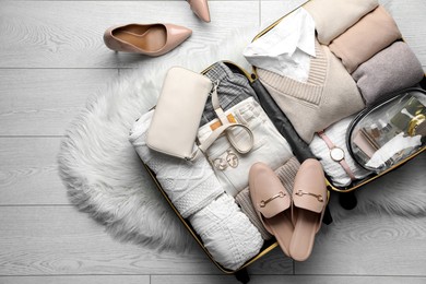 Open suitcase with folded clothes, shoes and accessories on floor, top view