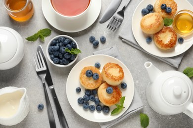 Delicious cottage cheese pancakes with blueberries, mint and honey served on light grey table, flat lay