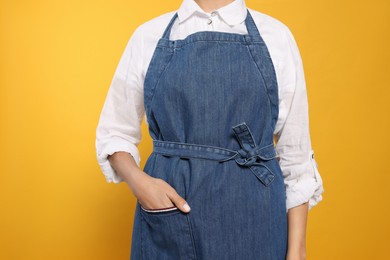 Young woman in blue jeans apron on yellow background, closeup