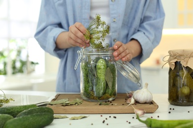 Woman putting dill into pickling jar at table in kitchen, closeup