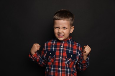 Photo of Angry little boy on black background. Aggressive behavior