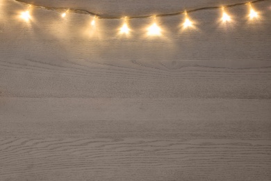 Beautiful glowing Christmas lights on white wooden table, top view. Space for text