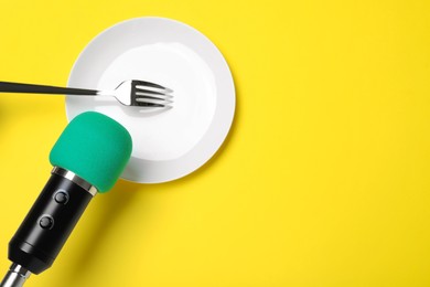 Making ASMR sounds with microphone, plate and fork on yellow background, flat lay. Space for text