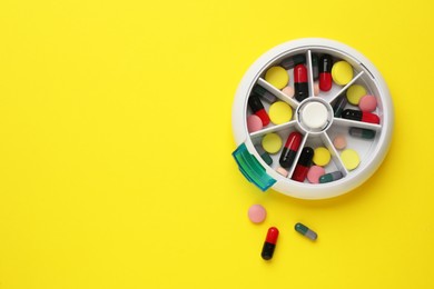 Plastic box with different pills on yellow background, flat lay. Space for text