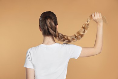 Photo of Teenage girl with strong healthy braided hair on beige background, back view