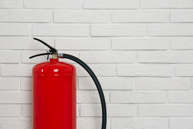 Fire extinguisher near white brick wall, closeup. Space for text