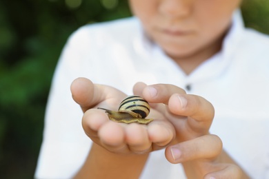 Boy playing with cute snail outdoors, closeup. Child spending time in nature