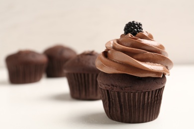 Delicious chocolate cupcake with cream and blackberry on white table, closeup. Space for text