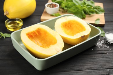 Raw spaghetti squash halves in baking dish and spices  on dark wooden table
