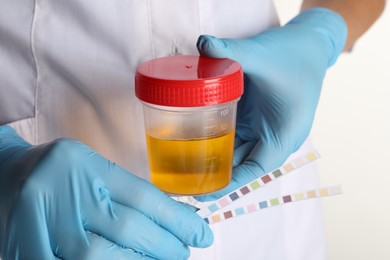 Photo of Nurse holding test strips and container with urine sample for analysis on white background, closeup