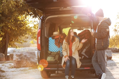 Young couple packing camping equipment into car trunk outdoors. Space for text