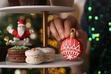 Photo of Woman taking Christmas macaron from stand against blurred festive lights, closeup