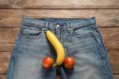 Men jeans with banana and nectarines symbolizing male genitals on wooden table, top view. Potency concept