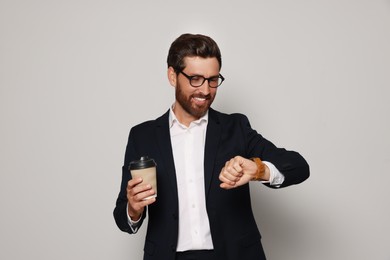Photo of Handsome bearded man with glasses and paper cup looking at wristwatch on light grey background