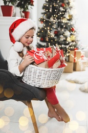 Image of Cute little girl in Santa hat with gifts from Christmas advent calendar at home. Bokeh effect