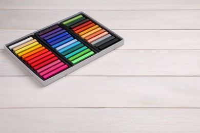 Set of colorful pastels in box on white wooden table, space for text. Drawing materials