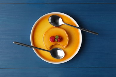 Photo of Delicious fresh pudding with caramel and raspberries on blue wooden table, top view