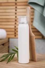 Dry shampoo spray, green leaves and comb on wooden table in bathroom