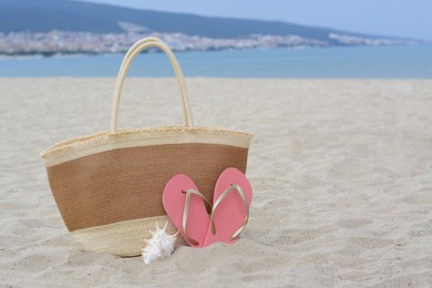 Stylish straw bag, flip flops and shell on sand near sea, space for text. Beach accessories