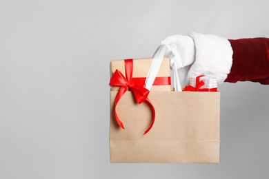 Santa holding paper bag with gift boxes on light grey background, closeup