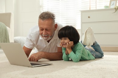 Happy grandfather and his grandson using laptop together on floor at home