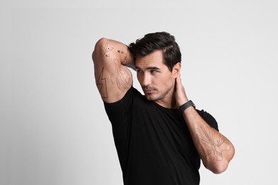 Handsome man with beautiful tattoo sketches on light grey background