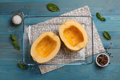 Raw spaghetti squash halves in glass baking dish with basil and spices on light blue wooden table, flat lay
