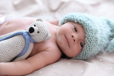 Cute newborn baby in warm hat with toy lying on bed