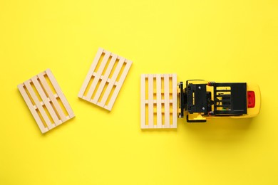 Toy forklift and wooden pallets on yellow background, flat lay